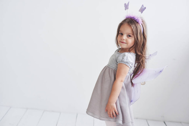 Side photo. Lovely little girl in the fairy costume standing in room with white background. - Foto, afbeelding