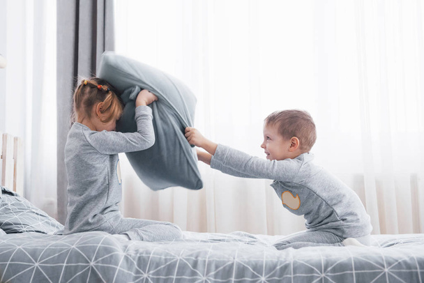 Kleine jongen en meisje geënsceneerd een kussengevecht op het bed in de slaapkamer. Stoute kinderen slaan elkaar kussens. Ze willen dat soort spel. - Foto, afbeelding