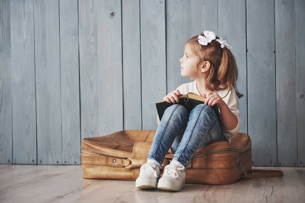 Ready to big travel. Happy little girl reading interesting book carrying a big briefcase and smiling. Travel, freedom and imagination concept. - Foto, Bild