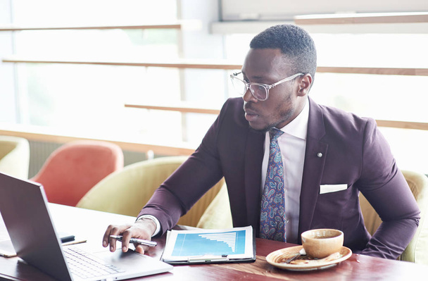 A beautiful stylish African American businesswoman wearing a suit uses his laptop while working - 写真・画像