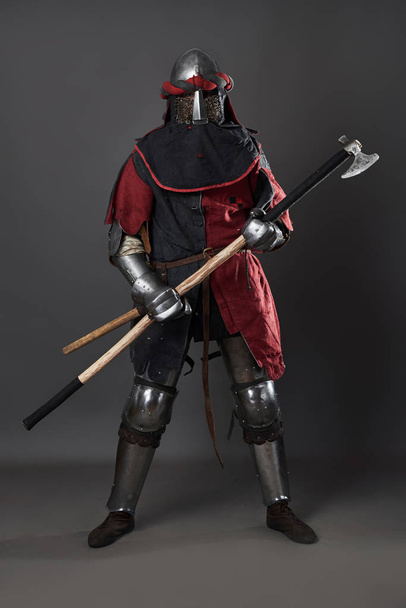 Medieval knight on grey background. Portrait of brutal dirty face warrior with chain mail armour red and black clothes and battle axe. - Foto, immagini