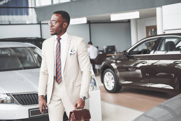 Young black businessman on auto salon background. Car sale and rent concept. - Foto, afbeelding