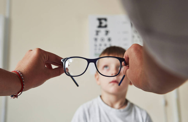 Focus on the specs. Doctor giving the child new black glasses for his vision. - Foto, imagen