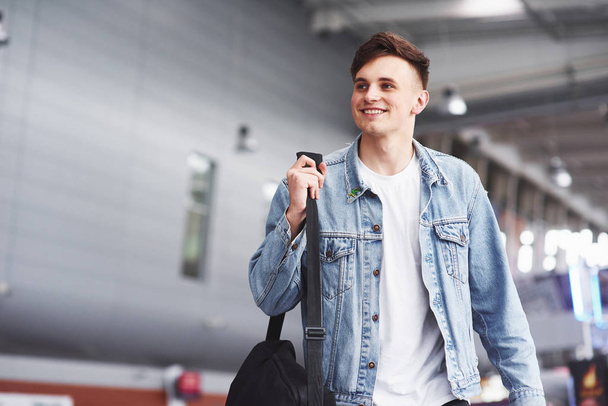 junger gutaussehender Mann mit einer Tasche auf der Schulter in Eile zum Flughafen. - Foto, Bild