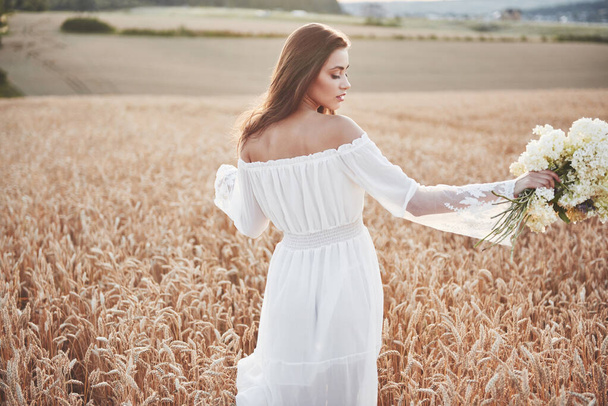 Beautiful girl in white dress running on the autumn field of wheat at sunset time - Foto, afbeelding