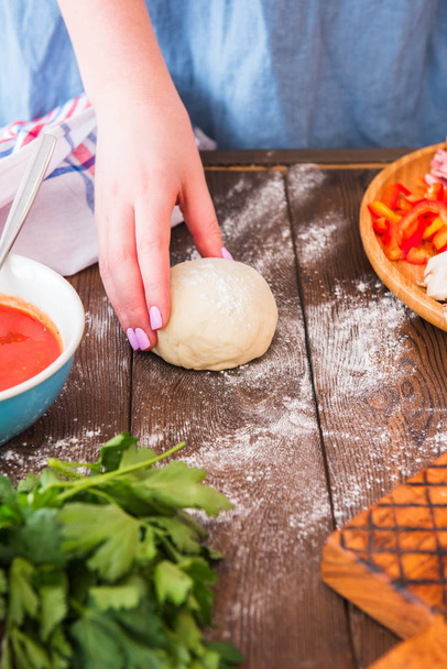 Raw dough in female hands, tomato sauce, food ingredients on a wooden table. - Photo, Image