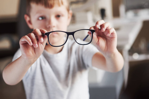 Focused photo. Little boy holds his new glasses in the doctor's office. - Φωτογραφία, εικόνα