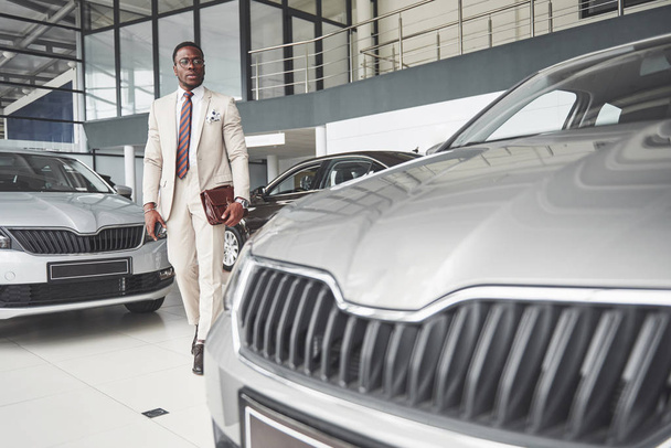 Young black businessman on auto salon background. Car sale and rent concept. Rich african american man. - Fotoğraf, Görsel