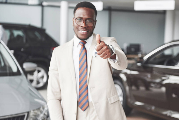 Young black businessman on auto salon background. Car sale and rent concept. - Foto, imagen