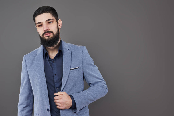 Portrait of freelancer man with beard in jacket standing against gray backdrop. - Foto, Imagen