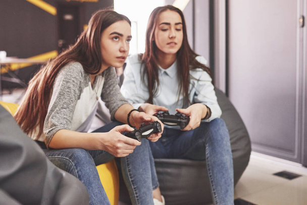 Twin sister sisters play on the console. Girls hold joysticks in their hands and have fun. - Fotó, kép