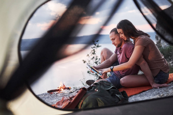 ハイキング中に湖の景色を横に地図を持つカップルのテントからの眺め。旅行ライフスタイルのコンセプトアドベンチャー休暇屋外. - 写真・画像