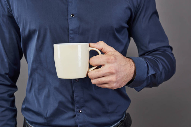 Handsome bearded man with stylish hair beard and mustache on serious face in shirt holding white cup or mug drinking tea or coffee in studio on grey background. - Foto, imagen