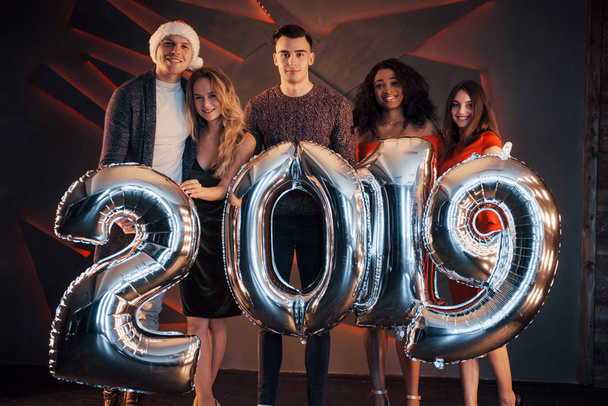 Het nieuwe 2019 nadert. Een groep vrolijke jonge multinationale mensen in Santa 's hoed met zilveren cijfers en confetti op het feest gooien. Gelukkig Nieuwjaar - Foto, afbeelding