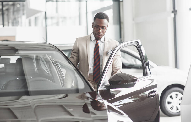 An African American inspects the car at the car dealership. Good bargain - Foto, Bild