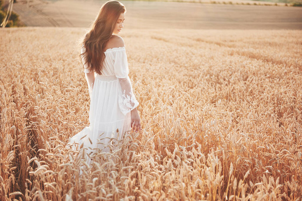 Happy young girl with long, beautiful hair standing in a wheat field under the sunlight. - Foto, immagini