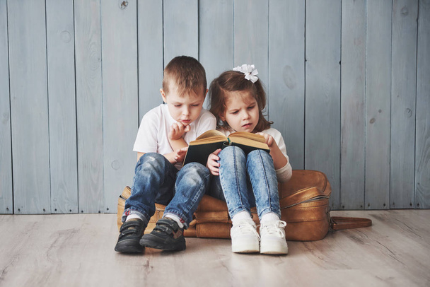 Ready to big travel. Happy little girl and boy reading interesting book carrying a big briefcase and smiling. Travel, freedom and imagination concept. - Foto, Imagen
