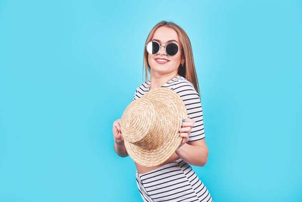 Attractive girl in a white and black stripes, hat, sunglasses, emotionally opened mouth on a bright blue background with a perfect body. Isolated. Studio shot. - Fotoğraf, Görsel