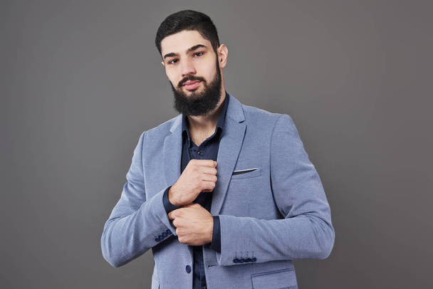 Portrait of freelancer man with beard in jacket standing against gray backdrop. - Foto, Bild