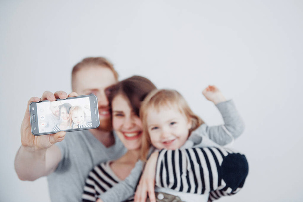 семья, праздники, технологии и люди - улыбающиеся мама, папа и маленькая девочка делают селфи с камерой на белом фоне
. - Фото, изображение