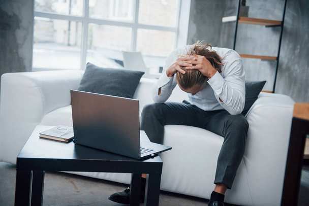 Stressed man sitting at couch in front of laptop have lowered his head. - Photo, image