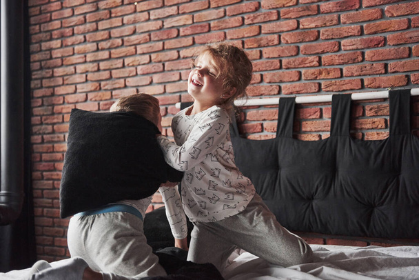 Niegrzeczne dzieci mały chłopiec i dziewczynka zainscenizował walkę na poduszki na łóżku w sypialni. Lubią takie gry.. - Zdjęcie, obraz