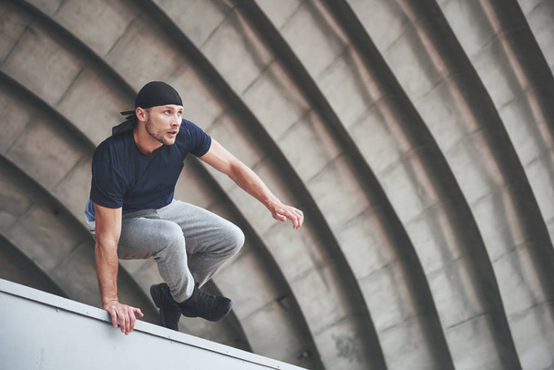 young man doing parkour jump in urban space in the city sunny spring summer day - 写真・画像