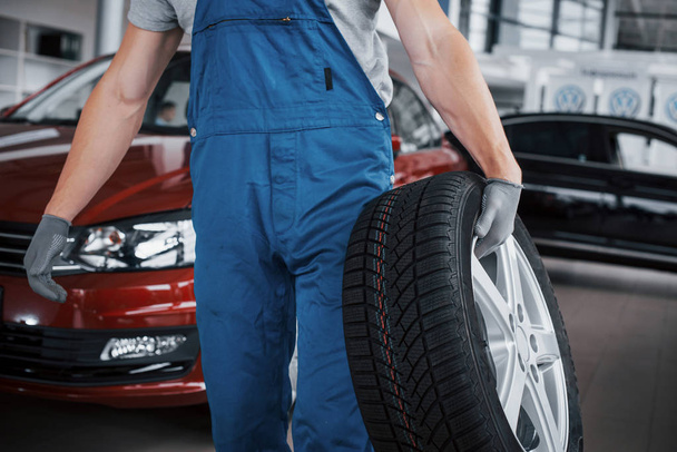 Mechanic holding a tire tire at the repair garage. replacement of winter and summer tires. - Foto, afbeelding