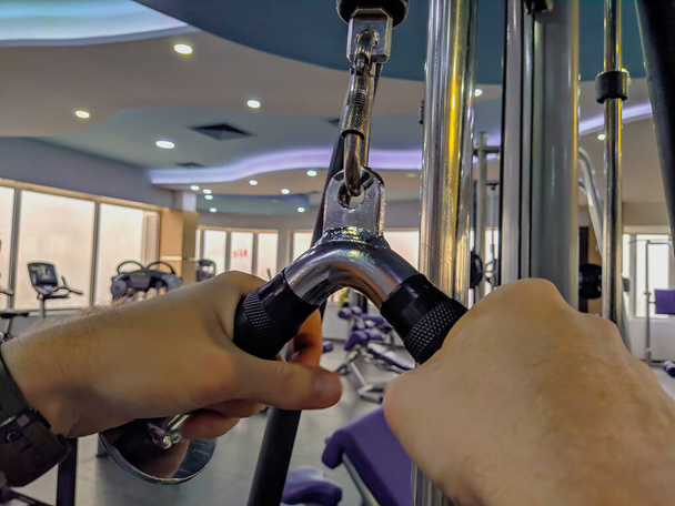 Κλείσιμο των χεριών του ανθρώπου τραβώντας το βάρος σε ένα σύγχρονο εσωτερικό γυμναστήριο, ενώ κάνει την άσκηση απώλειας βάρους και την αύξηση της δύναμης - Φωτογραφία, εικόνα
