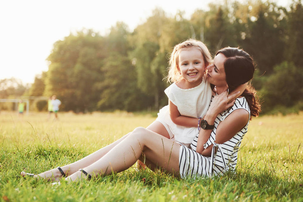 Happy mother and daughter hugging in a park in the sun on a bright summer background of herbs - Foto, afbeelding