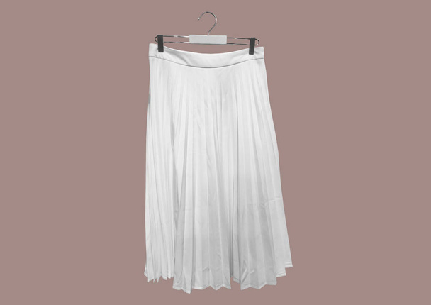 茶色の背景のパターンに隔離された白いプリーツロングスカート。女性の弾性ウエストバンドプレートレトロマキシロングスカートドレス。ロング・アコーディオン・プレートスカート。服の構成。フラットレイアウト、トップビュー - 写真・画像