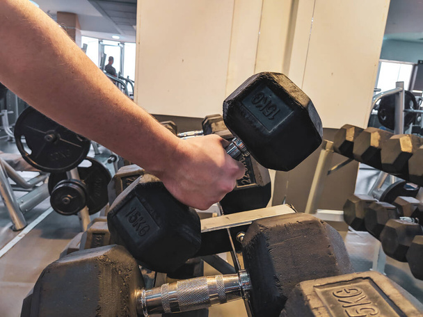 Erős felnőtt férfi kezét felvette egy súlyzó a szervezett sor nehéz súlyzó berendezések egy modern edzőteremben a súlyemelés és a növekvő erő - Fotó, kép
