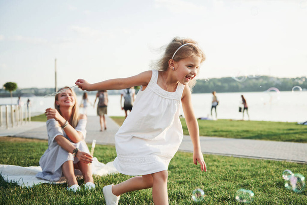 Egy csodálatos lány gyerek buborékokat csinál az anyjával a parkban. - Fotó, kép