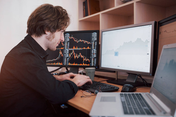 Stressful day at the office. Young businessman holding hands on his face while sitting at the desk in creative office. Stock Exchange Trading Forex Finance Graphic Concept. - Foto, Bild