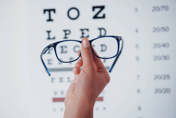 Woman hand holding the glasses on background of the eye chart. - Φωτογραφία, εικόνα