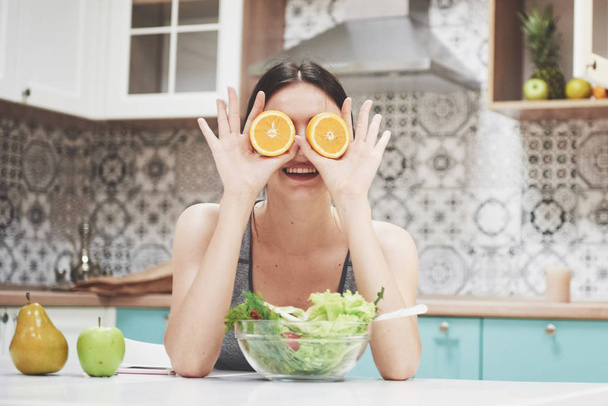 A young sports girl enjoys a fruit salad. Being playful covering her eyes with orange - Foto, immagini