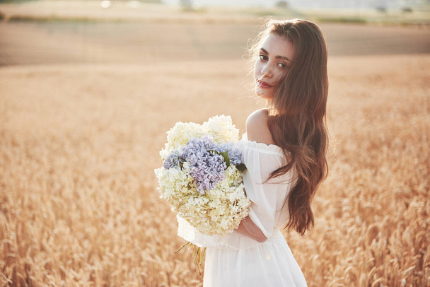 Beautiful girl in white dress running on the autumn field of wheat at sunset time - Фото, изображение