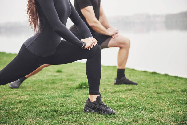 Fitness couple stretching outdoors in park near the water. Young bearded man and woman exercising together in morning. - Φωτογραφία, εικόνα