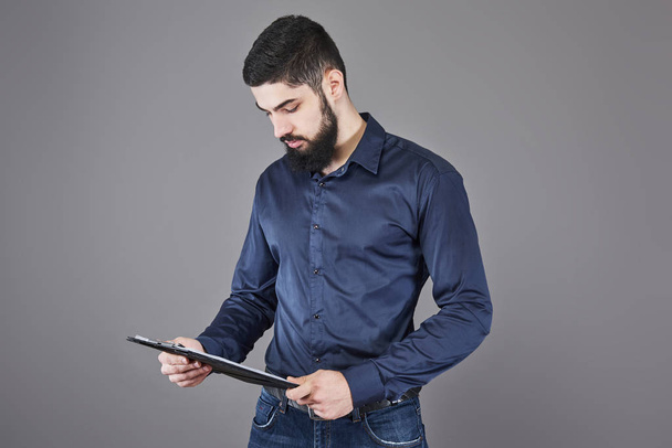Concentrated young attractive businessman in blue shirt planning and writing in clipboard. - Foto, imagen