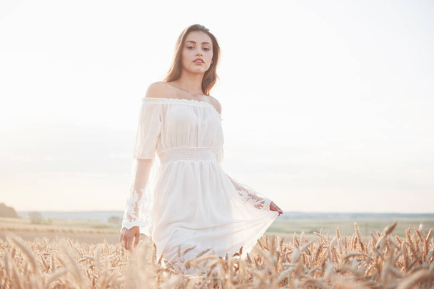 Portrait of a beautiful girl in a white dress in the field of wheat. - Photo, Image