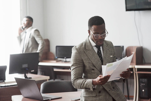 Het beeld van twee jonge Afro-Amerikaanse zakenlieden die op een vergadering in het kantoor met elkaar communiceren. - Foto, afbeelding