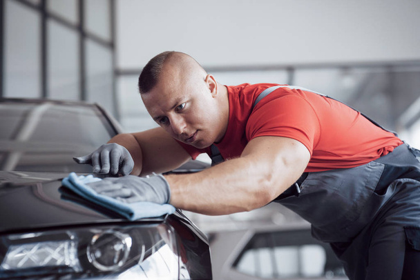 The man holds the microfiber in hand and polishes the car. The new machine is being prepared for sale. - 写真・画像
