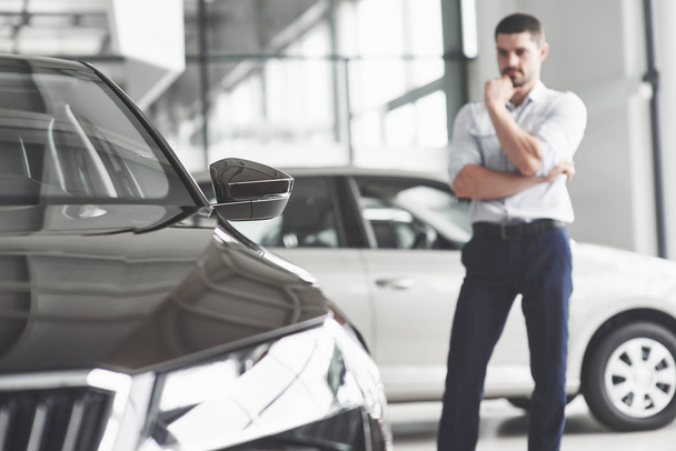 Handsome young man consultant at car salon standing near car - Photo, image