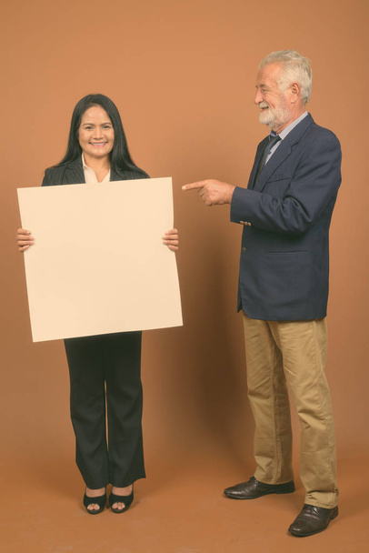 Studio shot of senior businessman and mature Asian businesswoman together against brown background - Foto, Bild