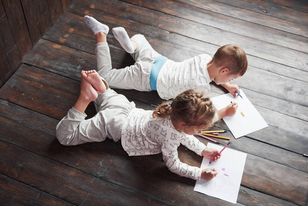 Kinder liegen im Schlafanzug auf dem Boden und zeichnen mit Bleistiften. Niedliche Kindermalerei mit Bleistift. - Foto, Bild