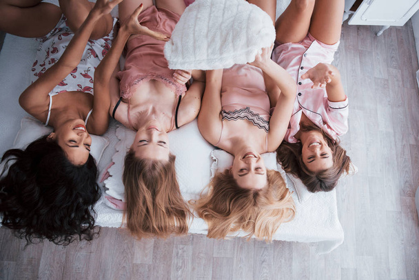Fun at bachelorette party. Inverted portrait of charming girls that lying on bed in nightwear. Top view. - Valokuva, kuva