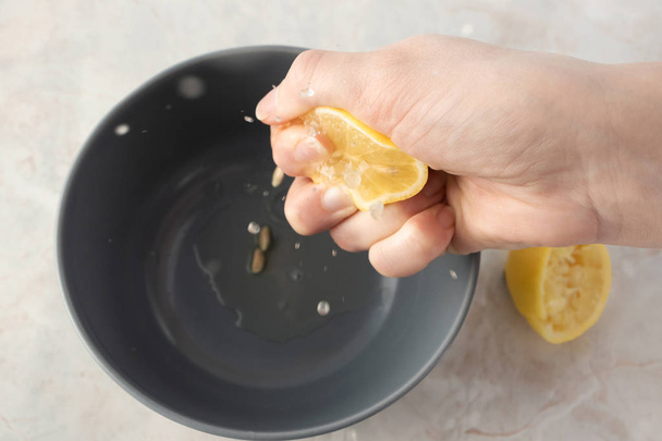 Жіноча рука стискає половину лимона над сірою мискою з соком на м
 - Фото, зображення