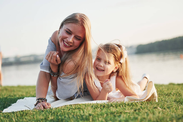 Atrakcyjne szczęśliwy młoda matka leżąca ze swoją uroczą córką na trawie w parku - Zdjęcie, obraz
