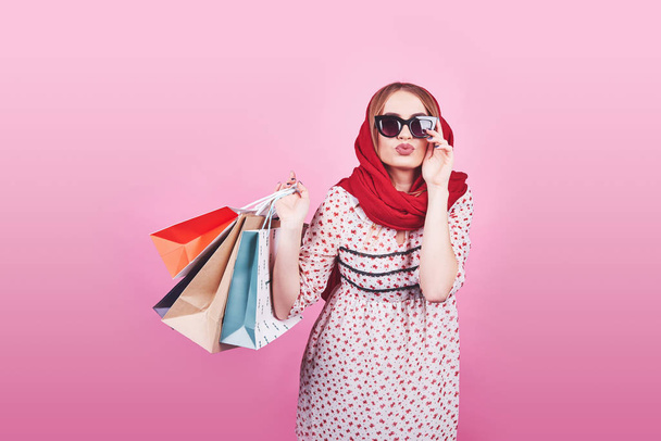 Portrait of young happy smiling woman with shopping bags on the pink Background. - 写真・画像