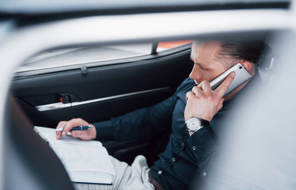 A young businessman arranges his affairs with a notepad while sitting in the car's back. - Foto, Bild